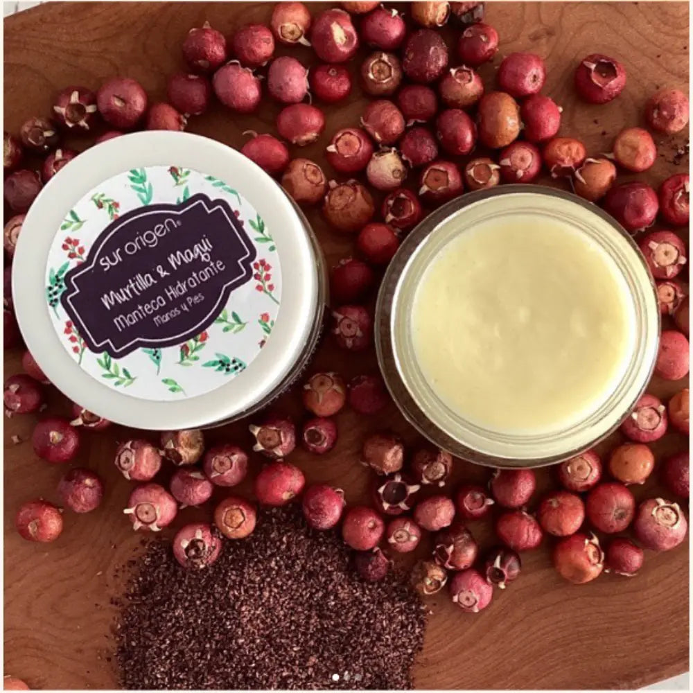 Envase abierto y cerrado de manteca hidratante “Murtilla & Maqui” de la marca Sur Origen, colocados sobre una superficie de madera rodeados de frutos rojos (murtilla) y polvo de maqui. La manteca en el frasco abierto muestra su textura cremosa, mientras el envase cerrado presenta un diseño floral en la tapa.