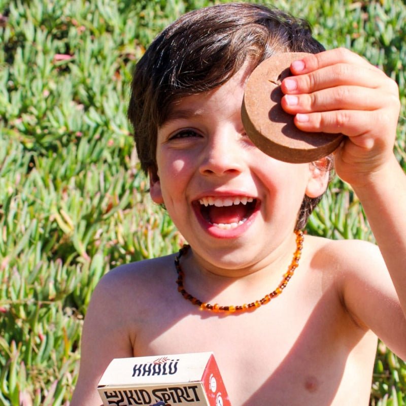 Niño sonriente al aire libre sosteniendo el champú sólido Smells Like Kid Spirit de Khalú, mostrando la caja y la barra en su mano.