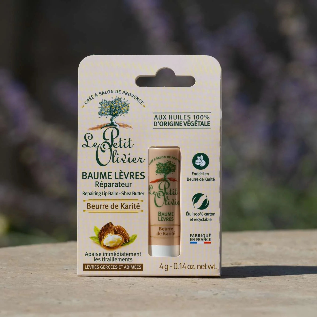Foto del bálsamo labial Le Petit Olivier en su empaque, apoyado sobre piedra con fondo natural desenfocado