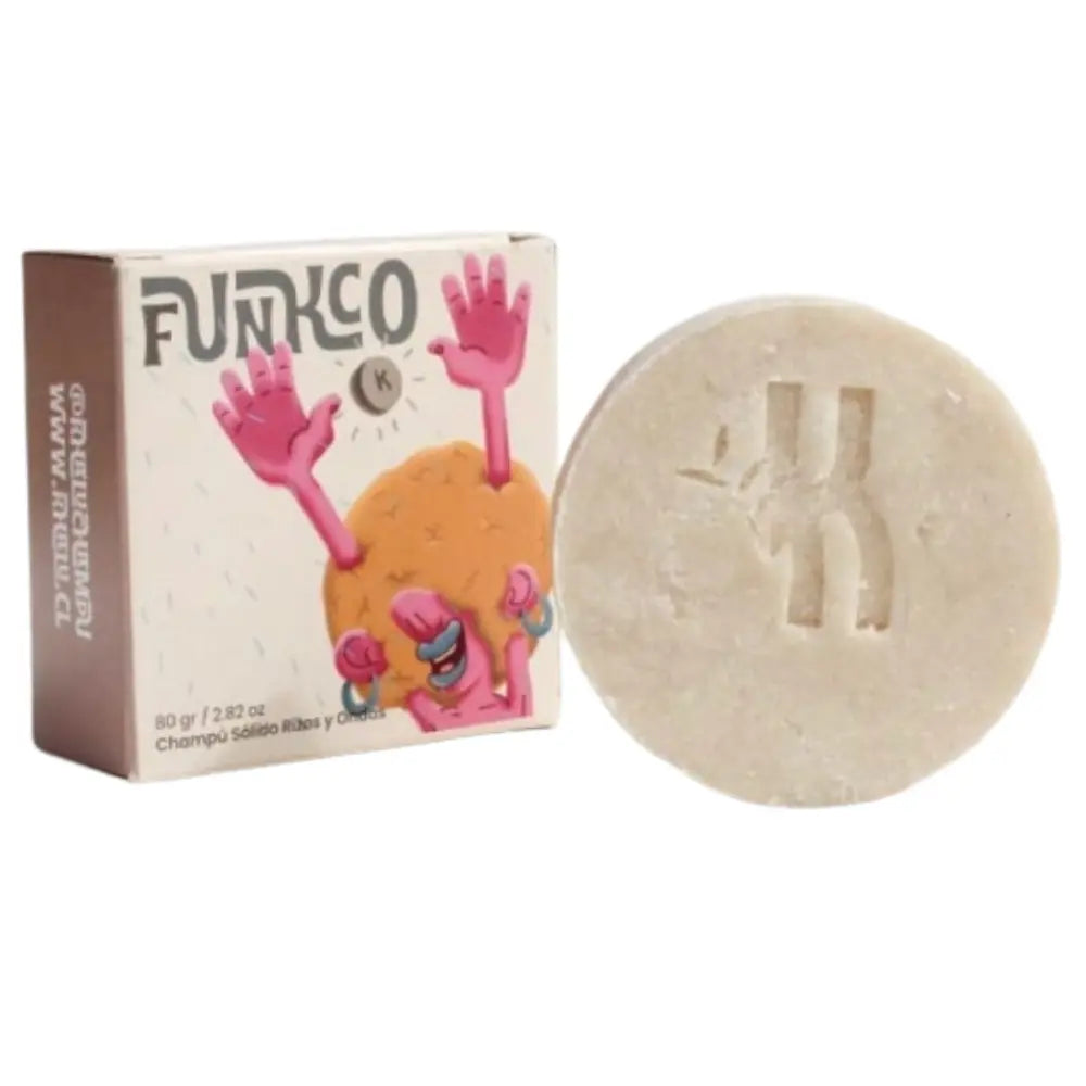 Fotografía de un champú sólido de 80 gramos de la marca Funko con aroma a ribes y cedro. A la izquierda se muestra la caja con diseño ilustrado y a la derecha el champú redondo con un logotipo en relieve.