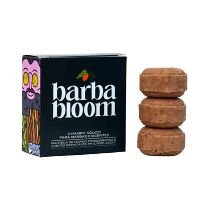 Imagen de un champú sólido para barba llamado “barba bloom”. A la izquierda se muestra la caja negra con ilustraciones coloridas en los costados y el texto: “Champú sólido para barbas exigentes. Manteca de mango, fitoqueratina & aceites esenciales. pH 5, 60g”. A la derecha, aparecen tres pastillas del champú apiladas una sobre otra, de color marrón claro con pequeñas partículas visibles, representando una textura natural.