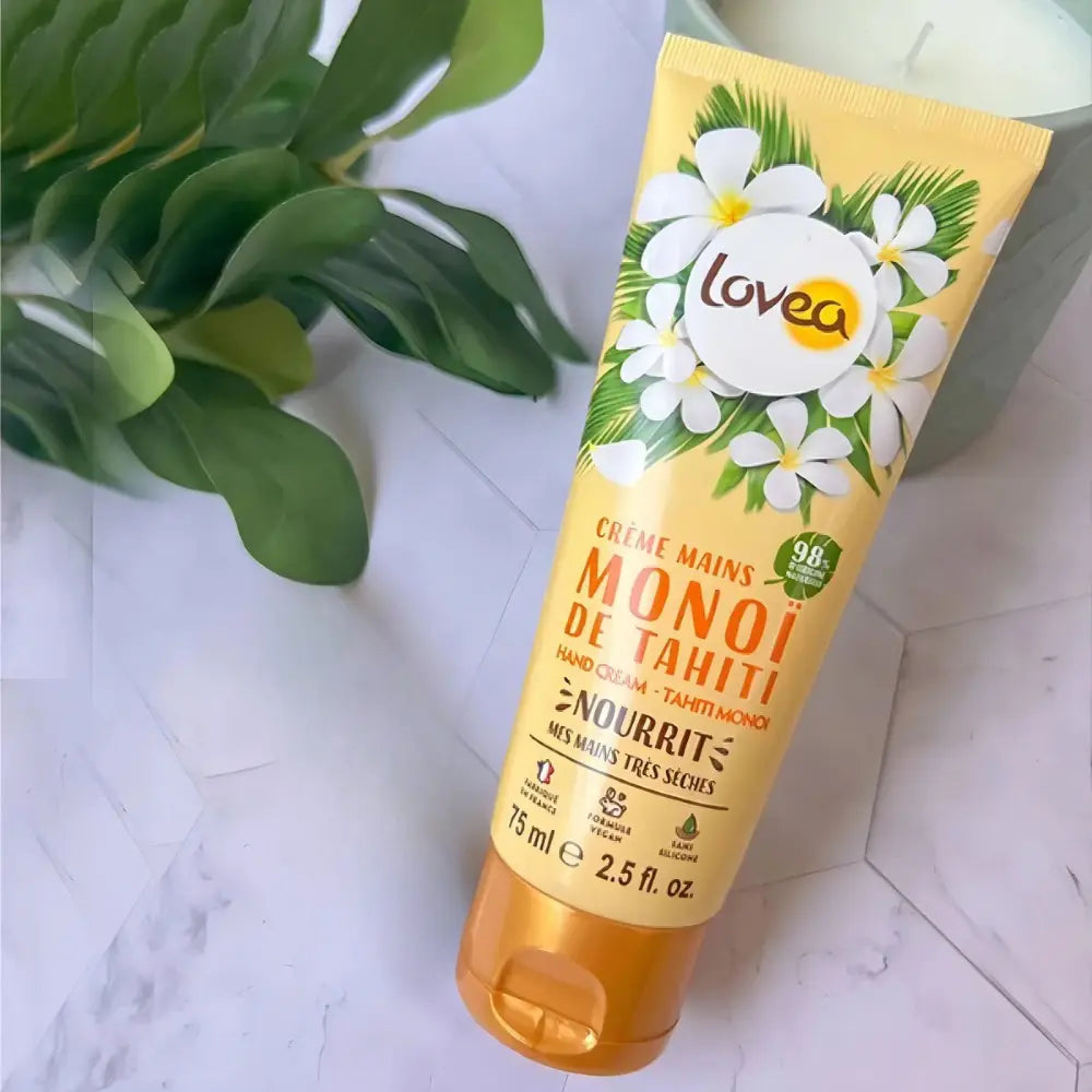 Crema de manos Lovea Monoi de Tahití 75 ml sobre superficie blanca y hojas verdes decorativas